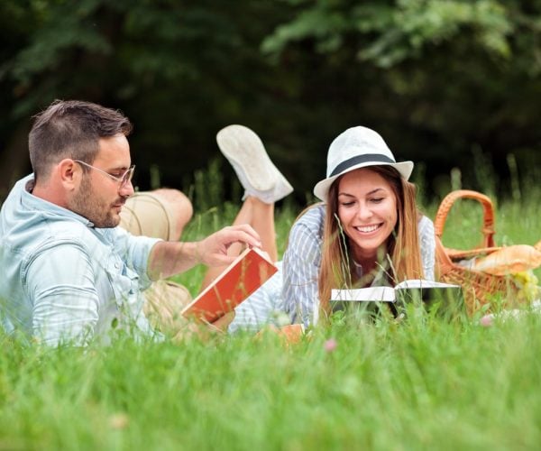 Beautiful young heterosexual couple having a great time during picnic in a park. Lying on a picnic blanket, reading books and relaxing