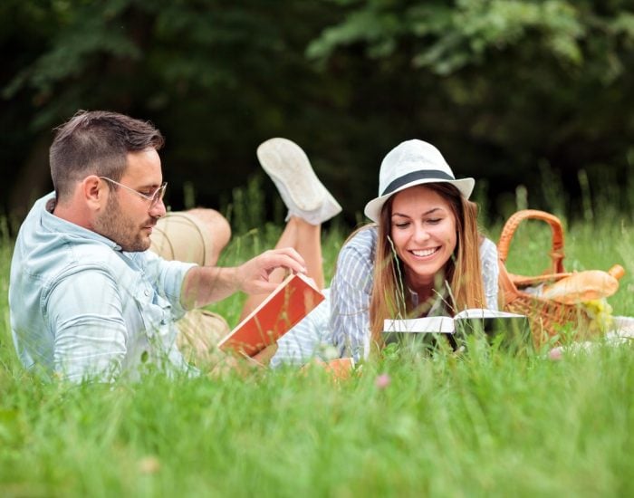 Beautiful young heterosexual couple having a great time during picnic in a park. Lying on a picnic blanket, reading books and relaxing