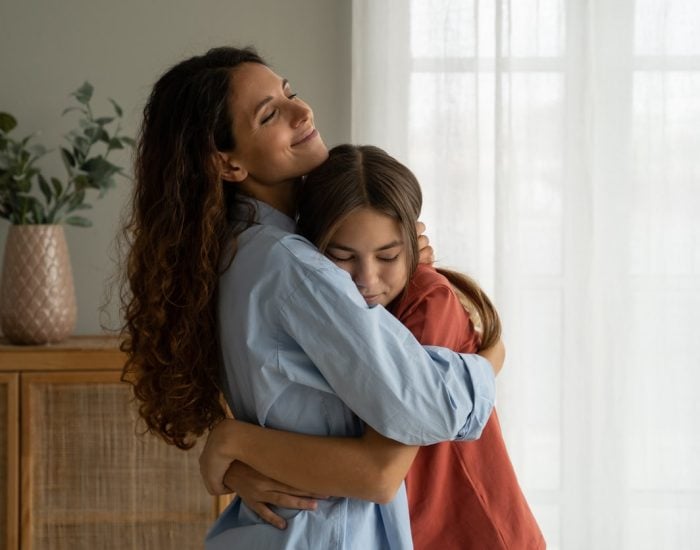 Young loving mother hugging her teenage daughter, mom demonstrating unconditional love for child, mommy cuddling supporting upset teen girl while spending time together at home. Mother-daughter bond