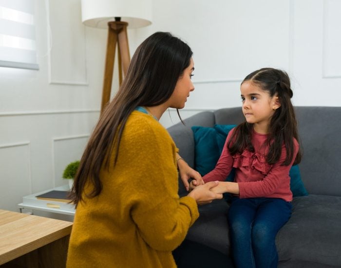Concerned loving mother talking to her young daughter about divorce and child custody while sitting on the sofa