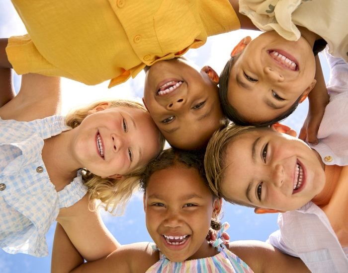 Group Of Multi-Cultural Children Friends Linking Arms Looking Down Into Camera
