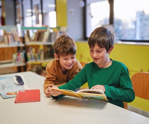 Two boys reading a book together in a library