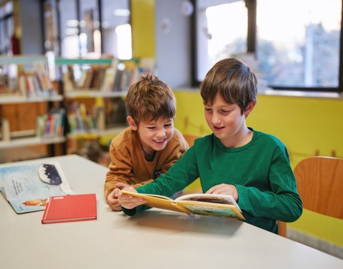 Two boys reading a book together in a library