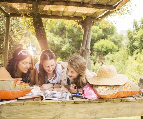 Three teenage girls reading magazine while lying in tree house in summer