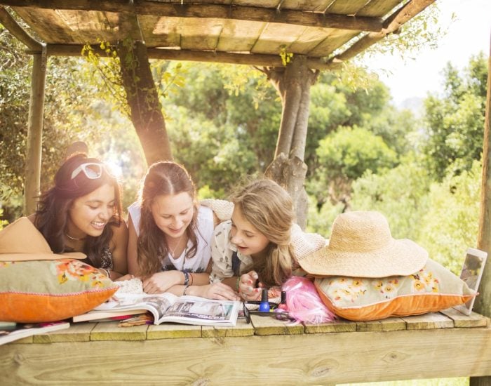 Three teenage girls reading magazine while lying in tree house in summer