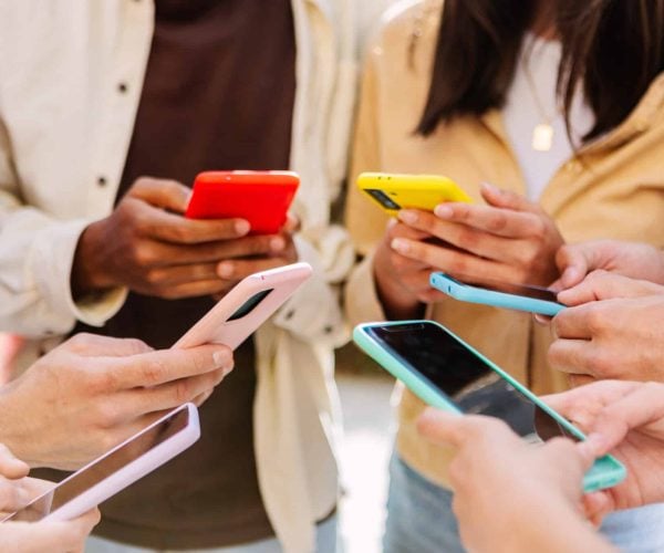 Closeup view of young group of people hands using mobile phone outdoors. Millennial people connected online browsing internet on smartphone device.